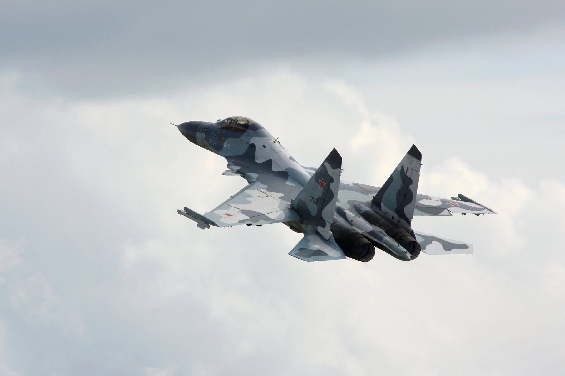 HD wallpaper of a military Sukhoi Su-30 warplane soaring through a cloudy sky, showcasing its sleek design and air force capabilities.