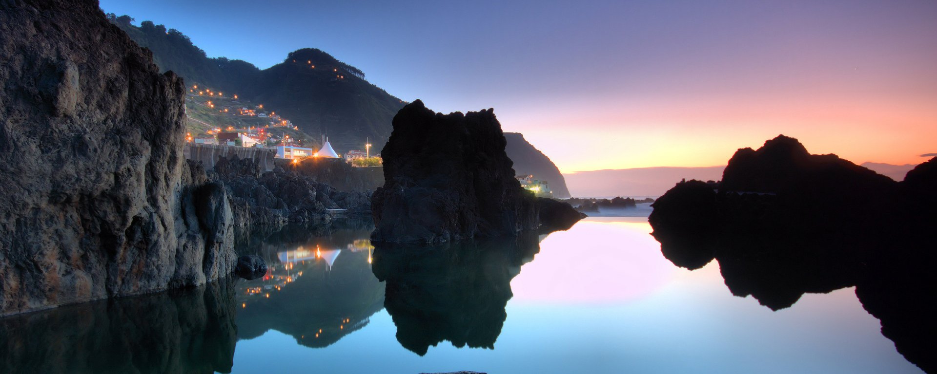 HD photography coastline PC desktop wallpaper and background: dusk view of rocky shoreline and silhouetted sea stacks reflected in glassy water, village lights twinkling under a fading sky.