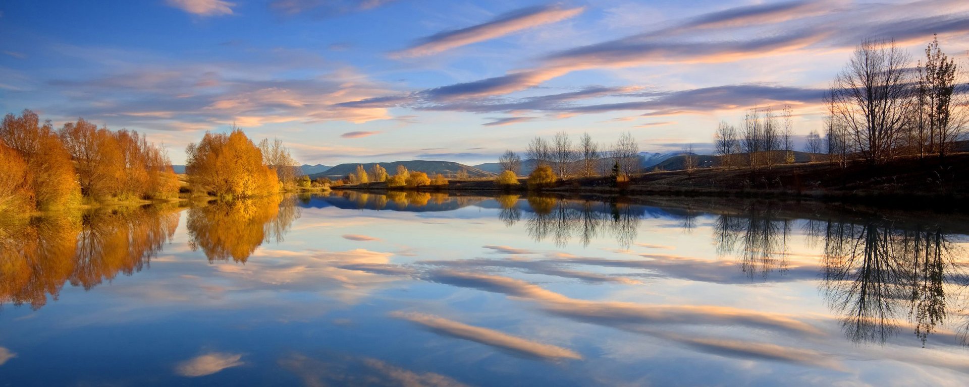 HD PC desktop wallpaper background: serene autumn lake at sunset, golden trees and pink-blue clouds mirrored in glassy water with distant hills along the horizon.