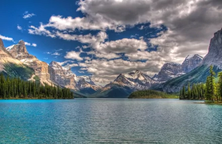 Scenic view of the Canadian Rockies featuring majestic mountains, a tranquil lake, and lush greenery, set under a vibrant sky. Ideal HD desktop wallpaper for nature enthusiasts.