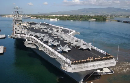 Aerial view of the USS John C. Stennis (CVN-74), a military aircraft carrier, docked with fighter jets on deck against a scenic backdrop, featured as an HD desktop wallpaper.