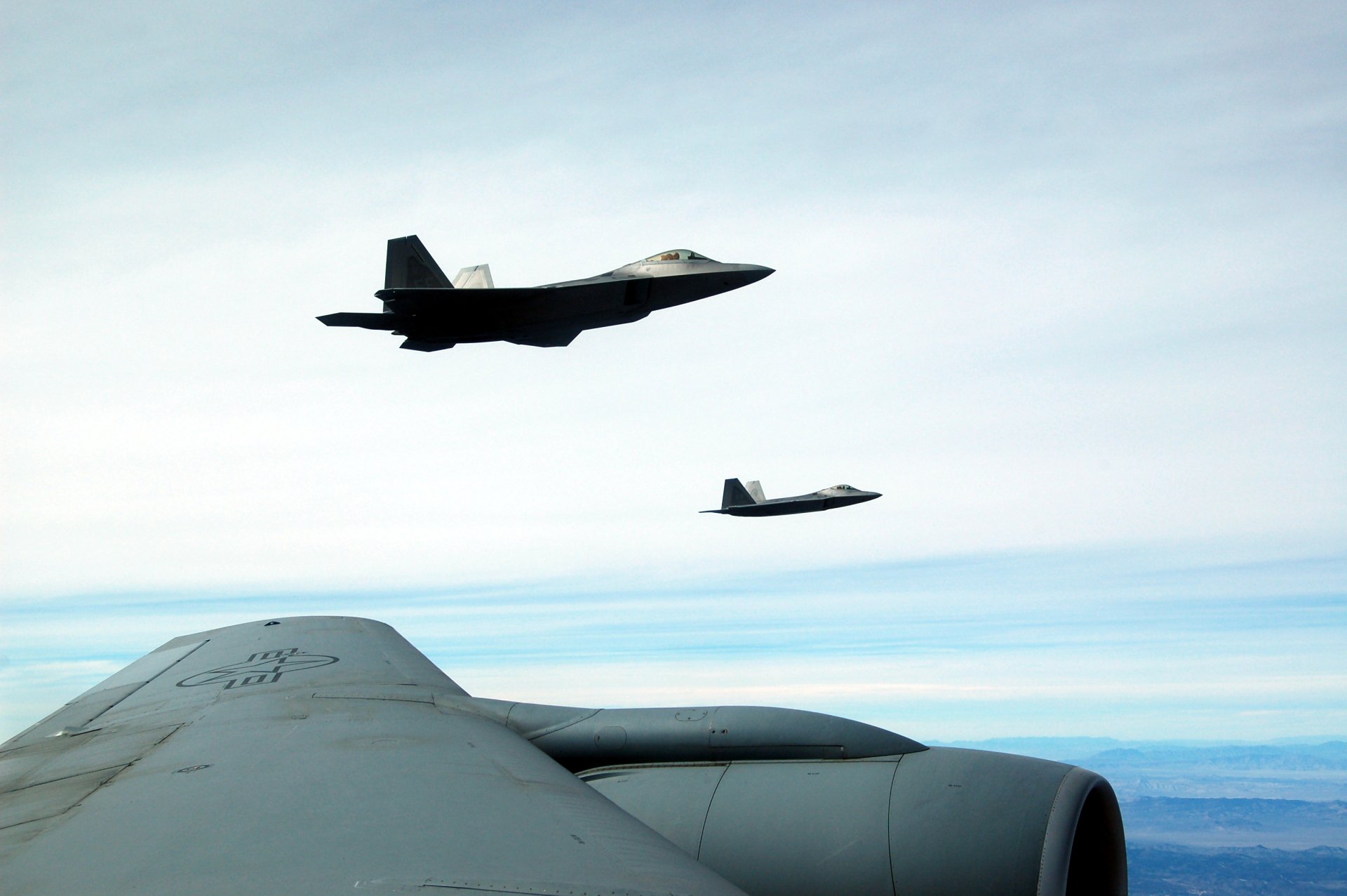 HD desktop wallpaper showing two military Lockheed Martin F-22 Raptor aircraft flying in clear skies above a large wing.