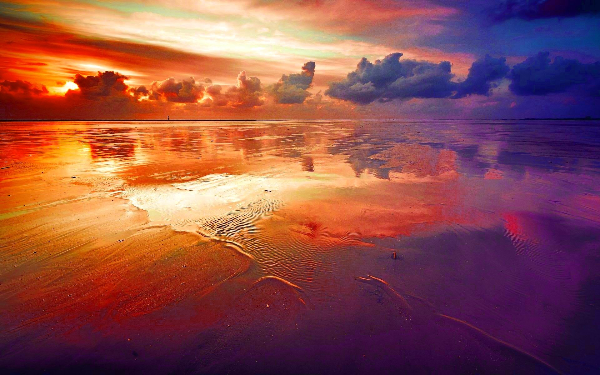 HD desktop wallpaper featuring a stunning sunset over a sandy beach, reflecting vibrant hues of orange, pink, and purple in the water and clouds. Natural, scenic background showcasing the beauty of nature.