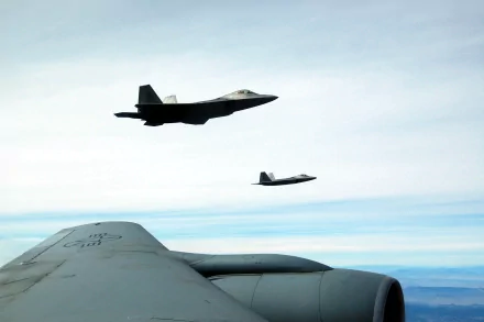 HD desktop wallpaper showing two military Lockheed Martin F-22 Raptor aircraft flying in clear skies above a large wing.