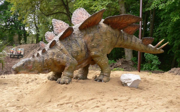 Animal — Stegosaurus statue on sandy ground beneath trees, textured plates and tail spikes; 2K Quad HD PC desktop wallpaper and background.