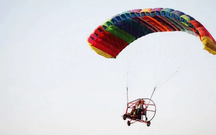 HD PC desktop wallpaper showing a colorful powered paraglider aircraft/vehicle soaring against a pale sky.