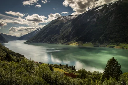 HD PC desktop wallpaper showcasing a stunning nature landscape with a serene lake surrounded by lush greenery and towering mountains under a partly cloudy sky.