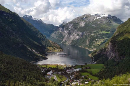 HD desktop wallpaper showcasing a man-made town nestled in a lush valley surrounded by towering mountains under a partly cloudy sky.