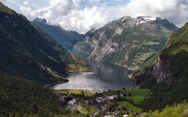 HD desktop wallpaper showcasing a man-made town nestled in a lush valley surrounded by towering mountains under a partly cloudy sky.