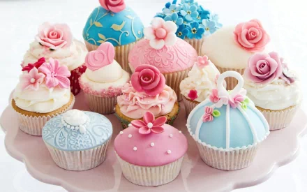 A colorful assortment of beautifully decorated cupcakes on a pink platter, featuring floral designs and intricate icing. This HD image serves as an appealing food-themed desktop wallpaper.
