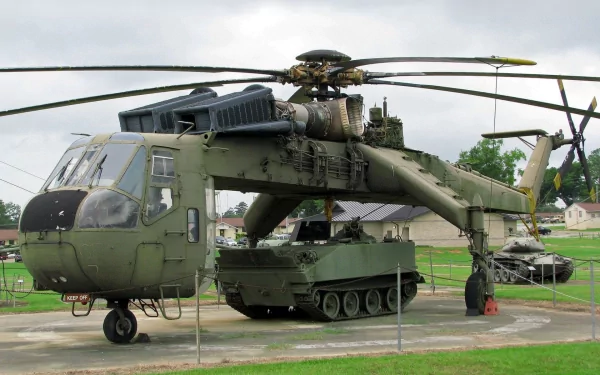 HD desktop wallpaper featuring a military Sikorsky CH-54 Tarhe helicopter with a tank displayed beneath it on a cloudy day.