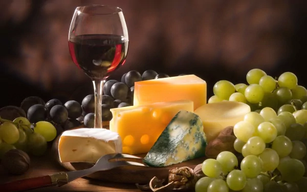 A HD desktop wallpaper featuring an elegant arrangement of various cheeses, a glass of red wine, and fresh grapes, creating a rich and inviting food theme.