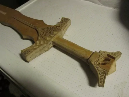 Fantasy weapon - carved wooden sword with ornate geometric hilt on a white surface, 4K Ultra HD PC desktop wallpaper and background.