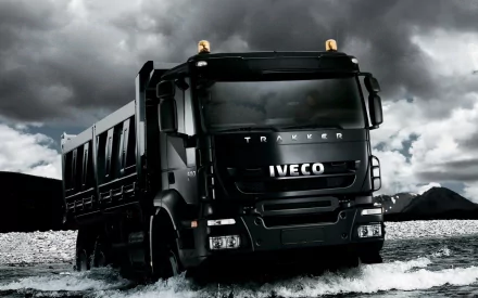 HD PC desktop wallpaper of an Iveco vehicle: black dump truck splashing through shallow water beneath dramatic storm clouds, high-contrast automotive background.