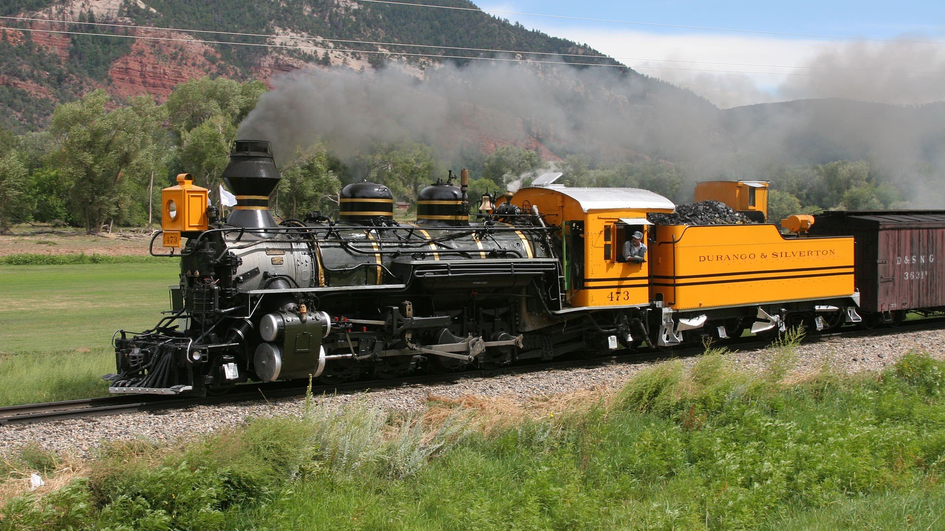HD desktop wallpaper featuring a vintage steam train traveling through a scenic green landscape with mountains in the background.