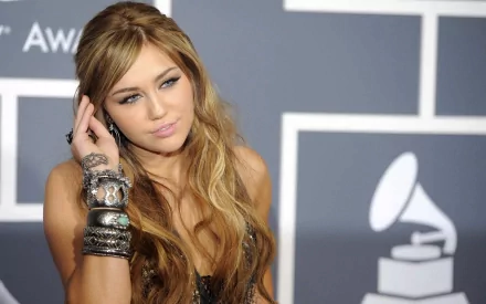 HD PC desktop wallpaper of a female pop singer at a music awards backdrop, long wavy hair and stacked bracelets, posing thoughtfully as a music-themed celebrity portrait.