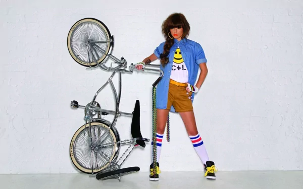 A vibrant HD wallpaper featuring Cher Lloyd posed confidently with a bicycle, dressed in a stylish outfit, capturing her unique music and fashion sense.