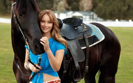 Jennifer Lawrence standing next to a black horse in a green field. This HD wallpaper captures the serene connection between the actress and the horse, providing a beautiful background image.