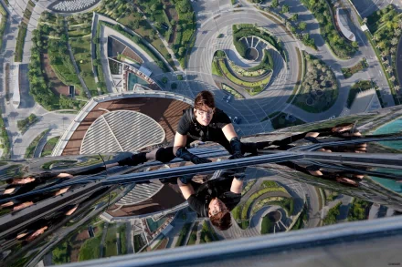 Ethan Hunt, played by Tom Cruise, scales a glass skyscraper in a dramatic scene from Mission: Impossible - Ghost Protocol. The image captures the sheer height and intensity, making it a gripping HD wallpaper.