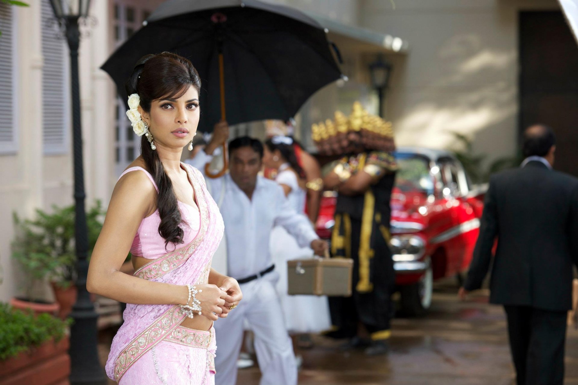 HD PC desktop wallpaper featuring celebrity Priyanka Chopra dressed in traditional attire, standing outdoors with a vintage car and crew in the background.