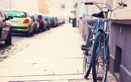 A stylish bicycle leans against a building, with parked cars lining the street in the background, creating a vibrant urban scene. An ideal HD desktop wallpaper and background.