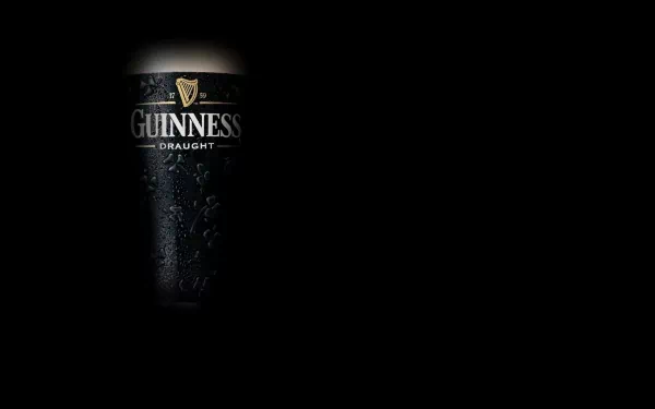 HD desktop wallpaper featuring a close-up of a cold, dark Guinness draught beer against a black background.