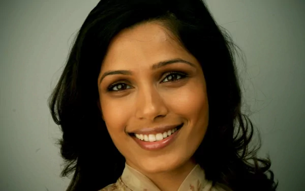 A close-up of Freida Pinto smiling warmly, showcasing her beautiful features and flowing hair, serves as an engaging HD desktop wallpaper and background.