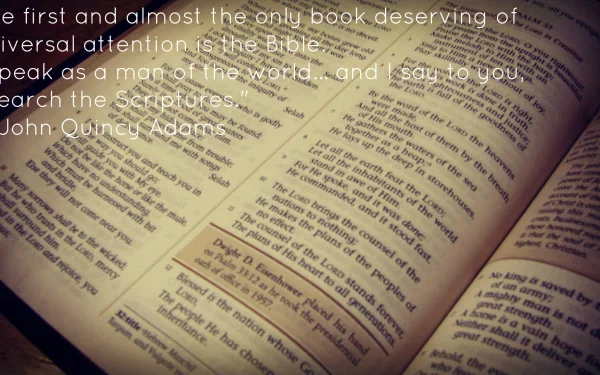 An HD desktop wallpaper featuring an open Bible with highlighted verses and text overlay of a John Quincy Adams quote advocating the importance of scriptures.