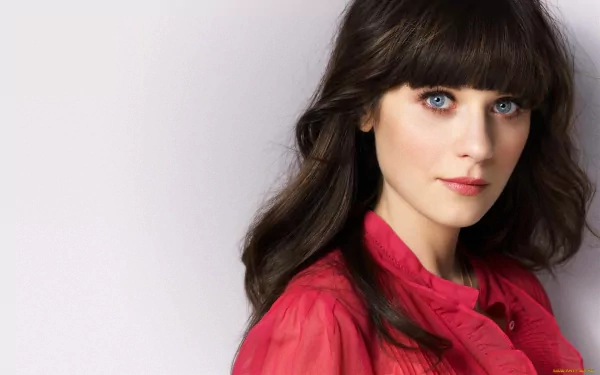 HD desktop wallpaper featuring Zooey Deschanel with striking blue eyes and long dark hair, wearing a vibrant red top against a soft background.