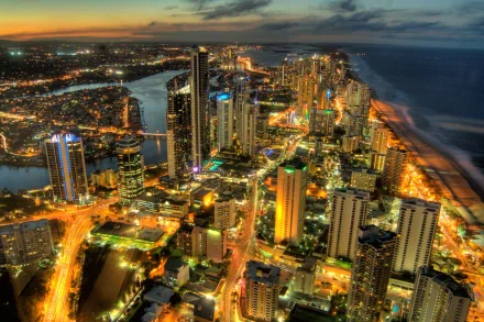 A stunning aerial view of Surfers Paradise, Gold Coast, Queensland, showcasing the vibrant city lights against the coastline at dusk. Man-made structures create a captivating skyline.