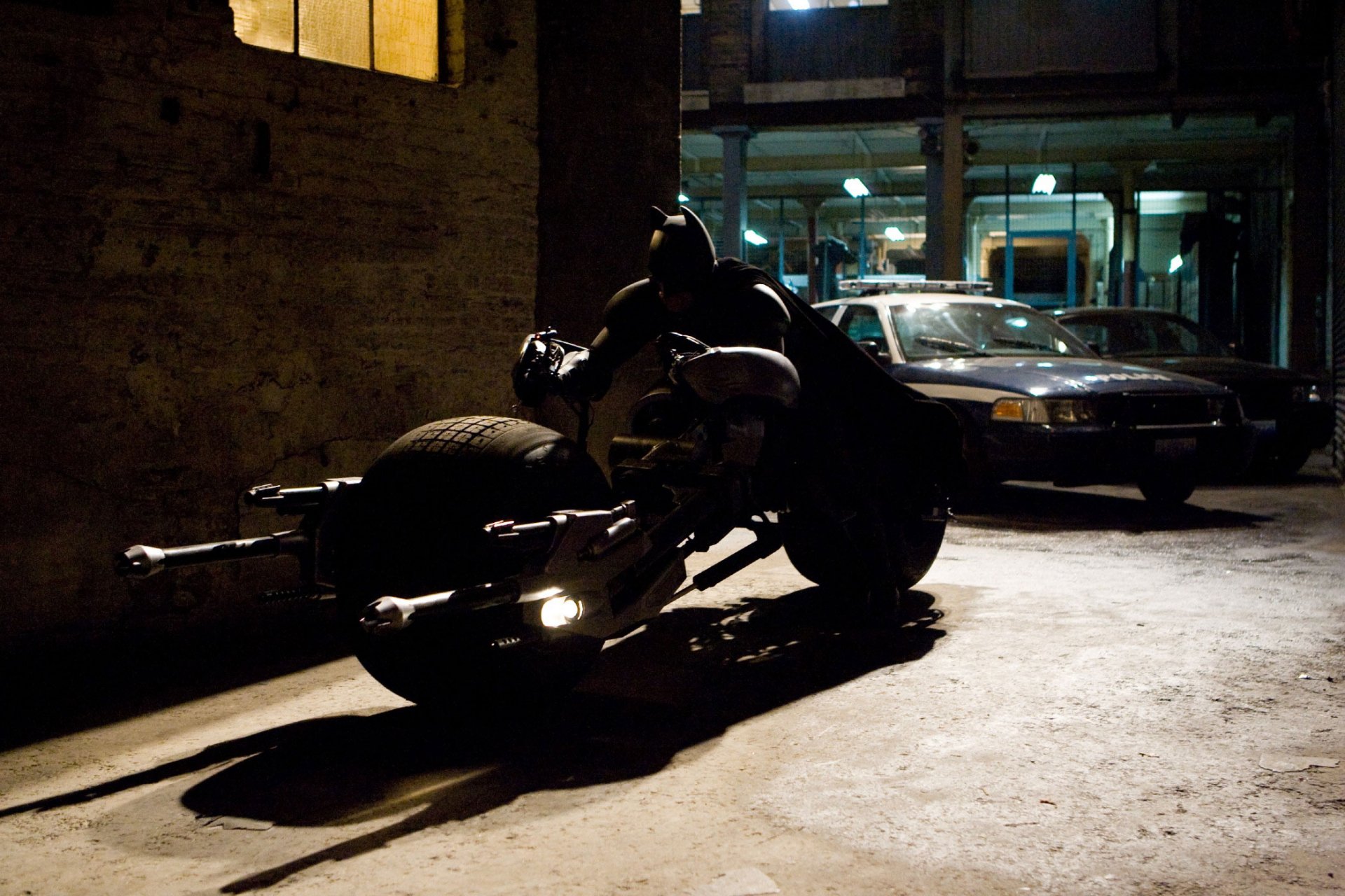 An HD wallpaper featuring Batman perched on his motorcycle in a dimly lit alley, capturing a moment from *The Dark Knight Rises*.