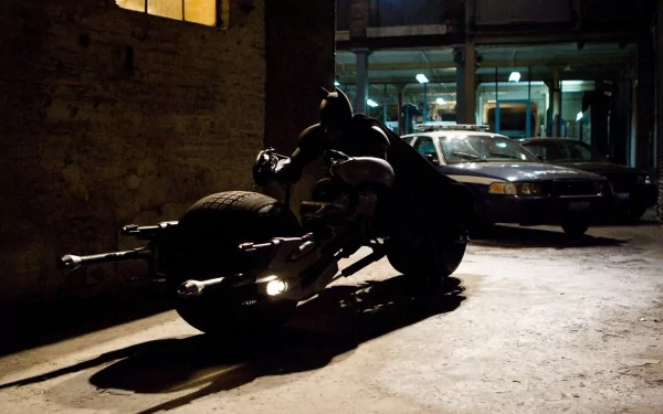An HD wallpaper featuring Batman perched on his motorcycle in a dimly lit alley, capturing a moment from *The Dark Knight Rises*.