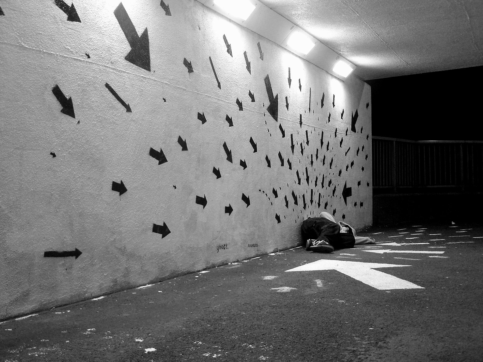 A black and white artistic wallpaper featuring a human figure resting against a wall adorned with scattered arrows, creating a striking contrast of movement and stillness.