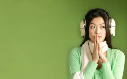 A captivating HD wallpaper of actress Jun Ji-hyun, featuring her with headphones, styled in a green sweater against a vibrant green background.