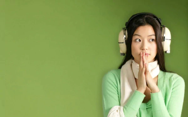 A captivating HD wallpaper of actress Jun Ji-hyun, featuring her with headphones, styled in a green sweater against a vibrant green background.