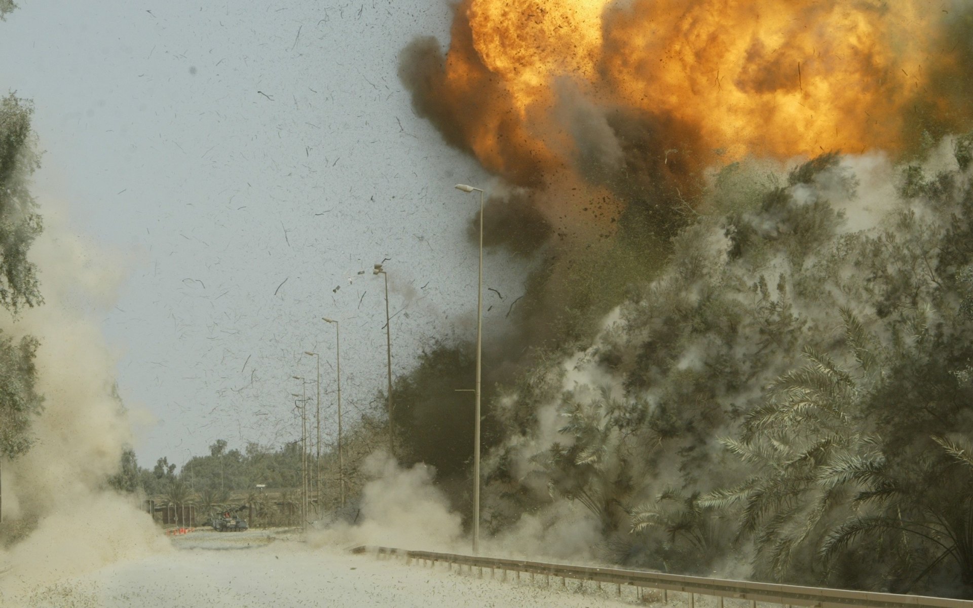 A dramatic explosion erupts near a road, surrounded by smoke and debris, capturing a powerful military scene. This high-definition image serves as an intense desktop wallpaper.