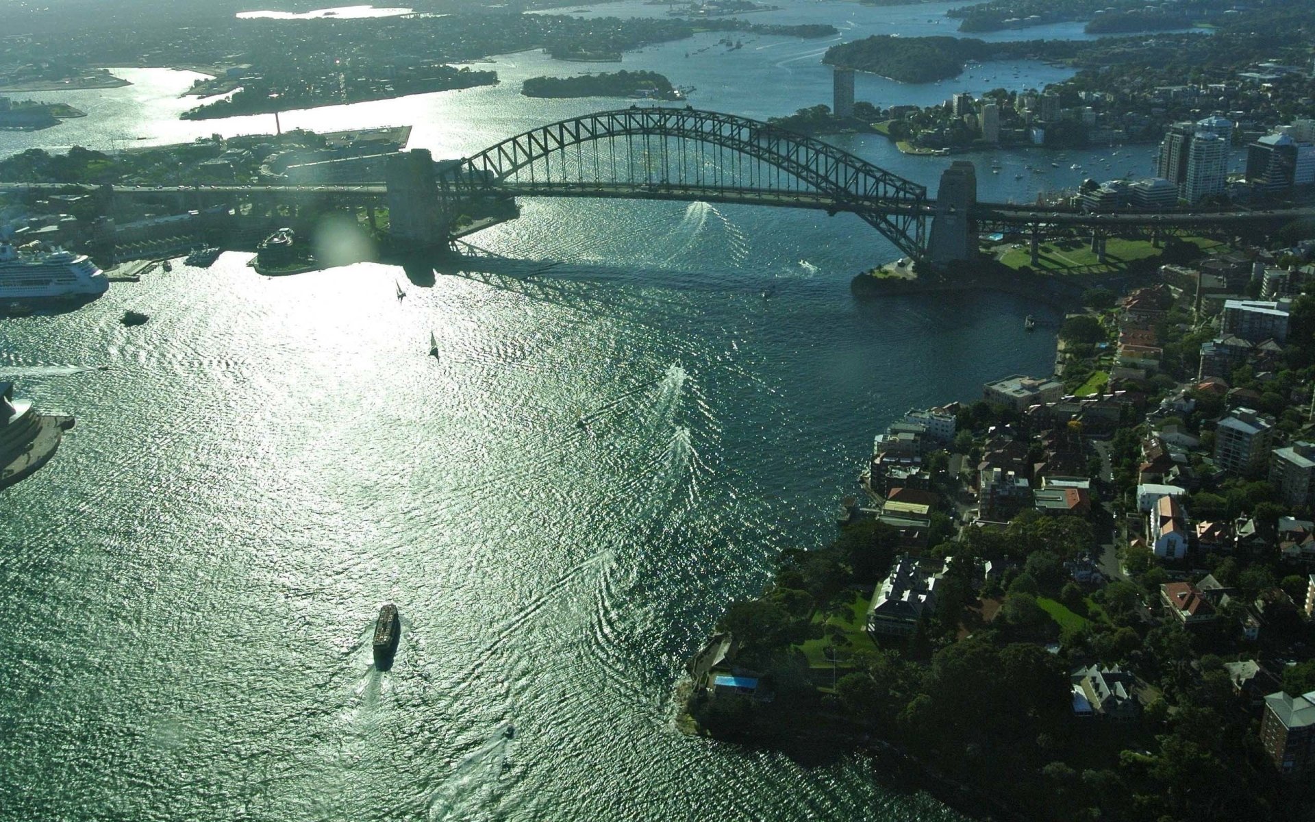 Aerial view of Sydney featuring the iconic man-made Sydney Harbour Bridge over shimmering water in an HD PC desktop wallpaper and background.