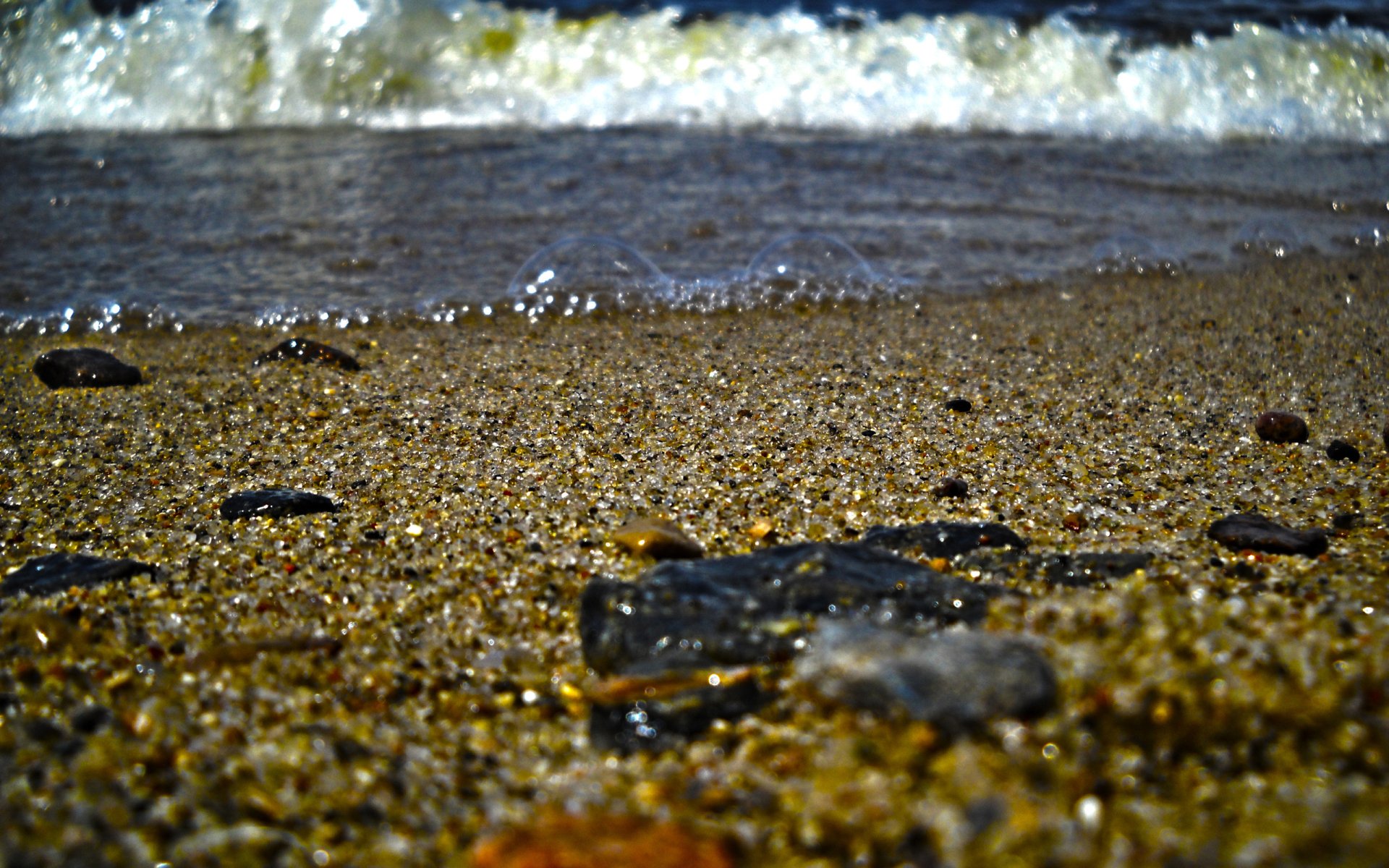 Close-up of stones and pebbled sand at the water’s edge with foamy waves — nature, stone; 2K Quad HD PC desktop wallpaper and background.