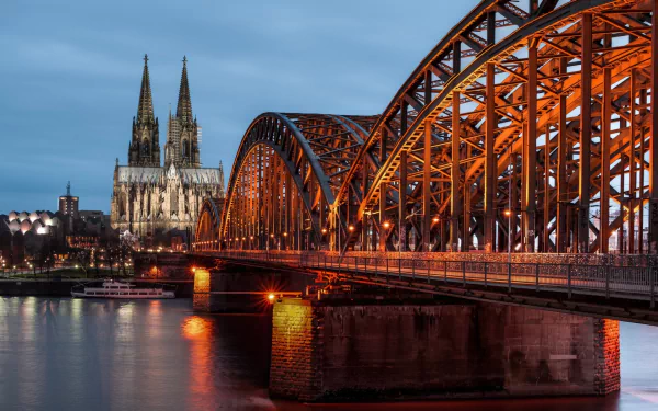HD desktop wallpaper showcasing the illuminated Hohenzollern Bridge spanning the Rhine River at dusk in Cologne, Germany, with the Cologne Cathedral in the background.
