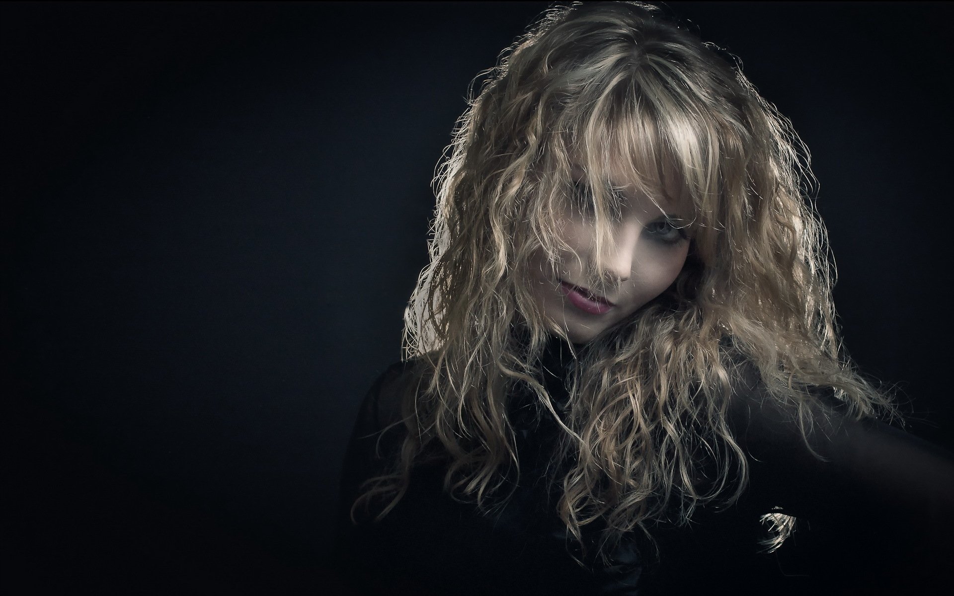 HD desktop wallpaper featuring a mysterious woman with curly blonde hair partially obscuring her face in a dim, moody lighting.