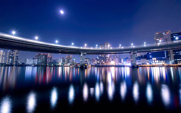 Night view of Tokyo's Rainbow Bridge illuminated over calm waters, with city lights reflecting beneath the curved man-made structure under a glowing moon.