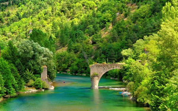 HD PC desktop wallpaper of a nature river scene: turquoise river flowing beneath a ruined stone bridge surrounded by dense, sunlit green forest.