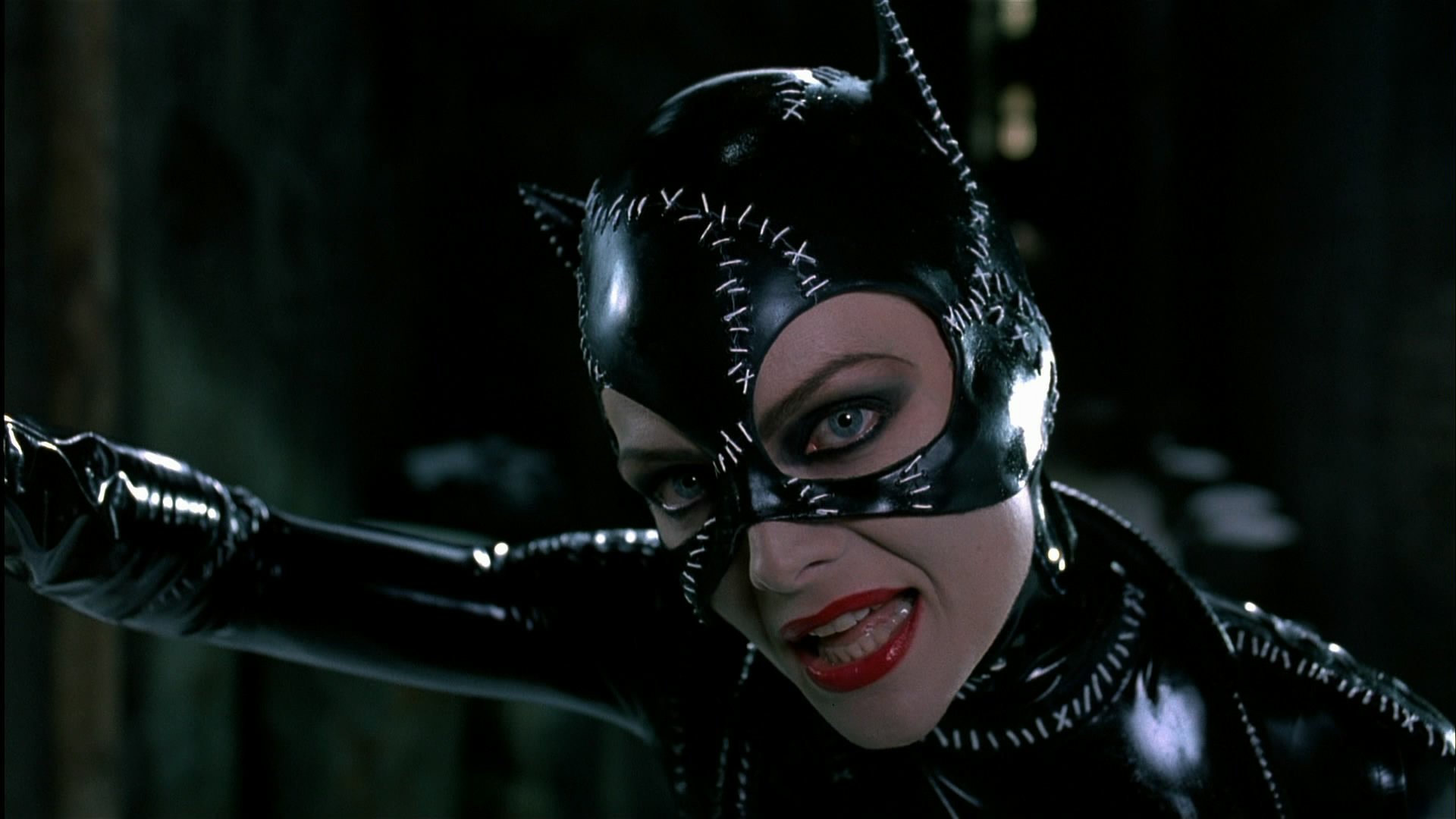Catwoman from the movie Batman Returns, close-up in a glossy stitched black catsuit, snarling with red lipstick — HD PC desktop wallpaper/background.