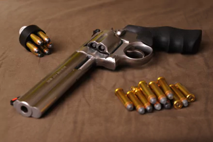 A high-definition desktop wallpaper featuring a Smith & Wesson revolver, surrounded by bullets and a speedloader on a neutral background.