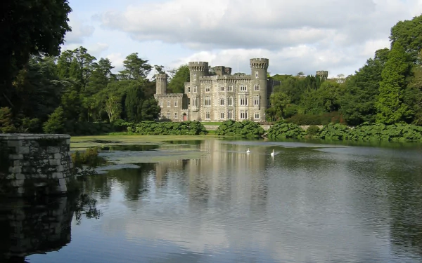 HD desktop wallpaper showcasing Johnstown Castle, a historic man-made structure surrounded by greenery and reflected in a serene lake under a partly cloudy sky.