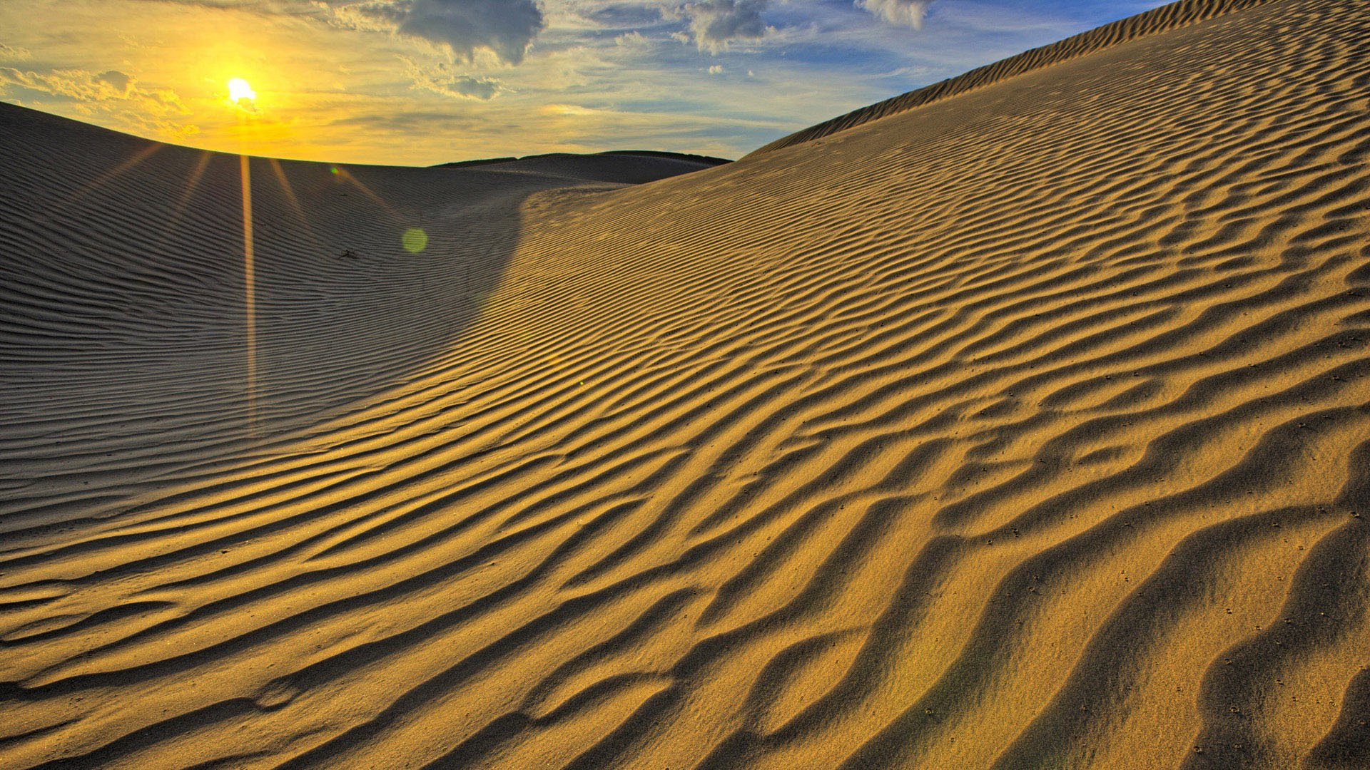HD PC desktop wallpaper featuring sunlit desert sand dunes under a partly cloudy sky, highlighting the natural patterns and textures of the sandy landscape.