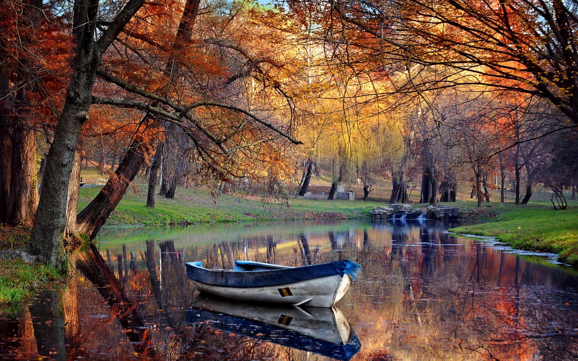 A serene fall scene featuring a tranquil lake with vibrant autumn foliage and a boat gently bobbing on the water, creating a peaceful HD desktop wallpaper.