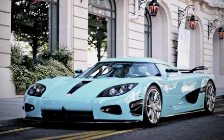 A sleek turquoise Koenigsegg Agera R parked elegantly on a city street in front of a stylish building, featured as a high-definition desktop wallpaper and background.