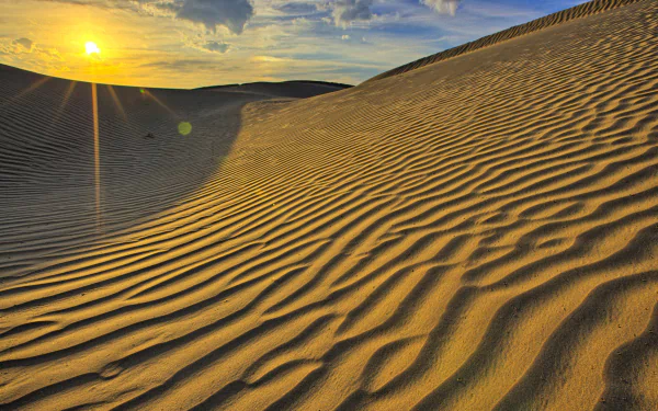 HD PC desktop wallpaper featuring sunlit desert sand dunes under a partly cloudy sky, highlighting the natural patterns and textures of the sandy landscape.