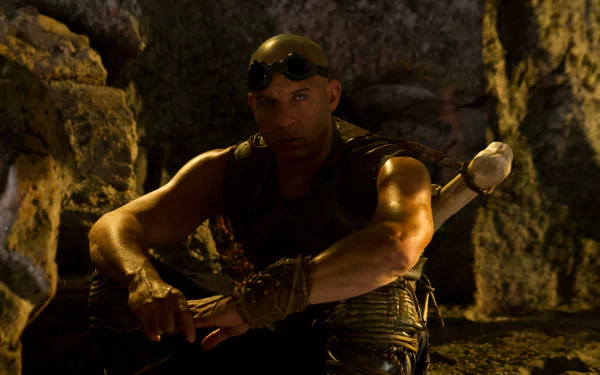 HD desktop wallpaper of a character from Riddick, seated in a rocky setting, wearing goggles and tactical gear.
